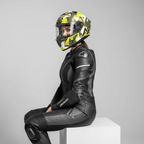 Figura in tuta di pelle nera seduta di profilo con il casco Airoh Valor Army, in studio