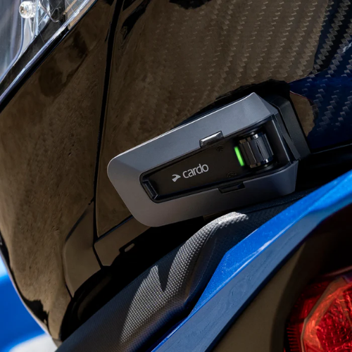 Cardo Packtalk Edge montato sul casco di un motociclista accanto alla moto