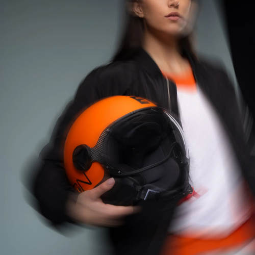 Casco jet Momo Design FGTR Classic Mono arancione opaco tenuto in mano, ambientazione su fondo scuro