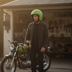 Uomo col casco jet Vespa Colors verde opaco davanti a un garage con una moto classica