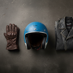 Casco jet Vespa Heritage azzurro appoggiato accanto a guanti in pelle marrone e giacca in pelle nera