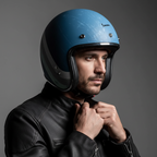 Uomo con giacca in pelle nera indossa il casco jet Vespa Heritage azzurro e allaccia il cinturino