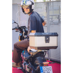 Motociclista che carica un casco nel bauletto Kappa in alluminio montato sul portapacchi di uno scooter