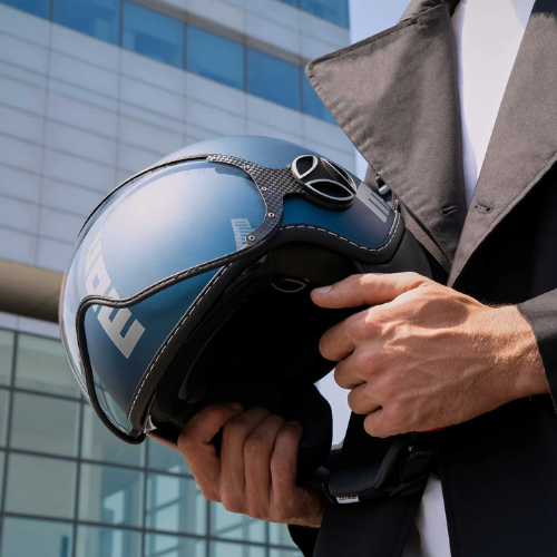 Dettaglio del casco jet Momo Design FGTR EVO blu avio opaco/silver tenuto in mano davanti a un edificio in vetro